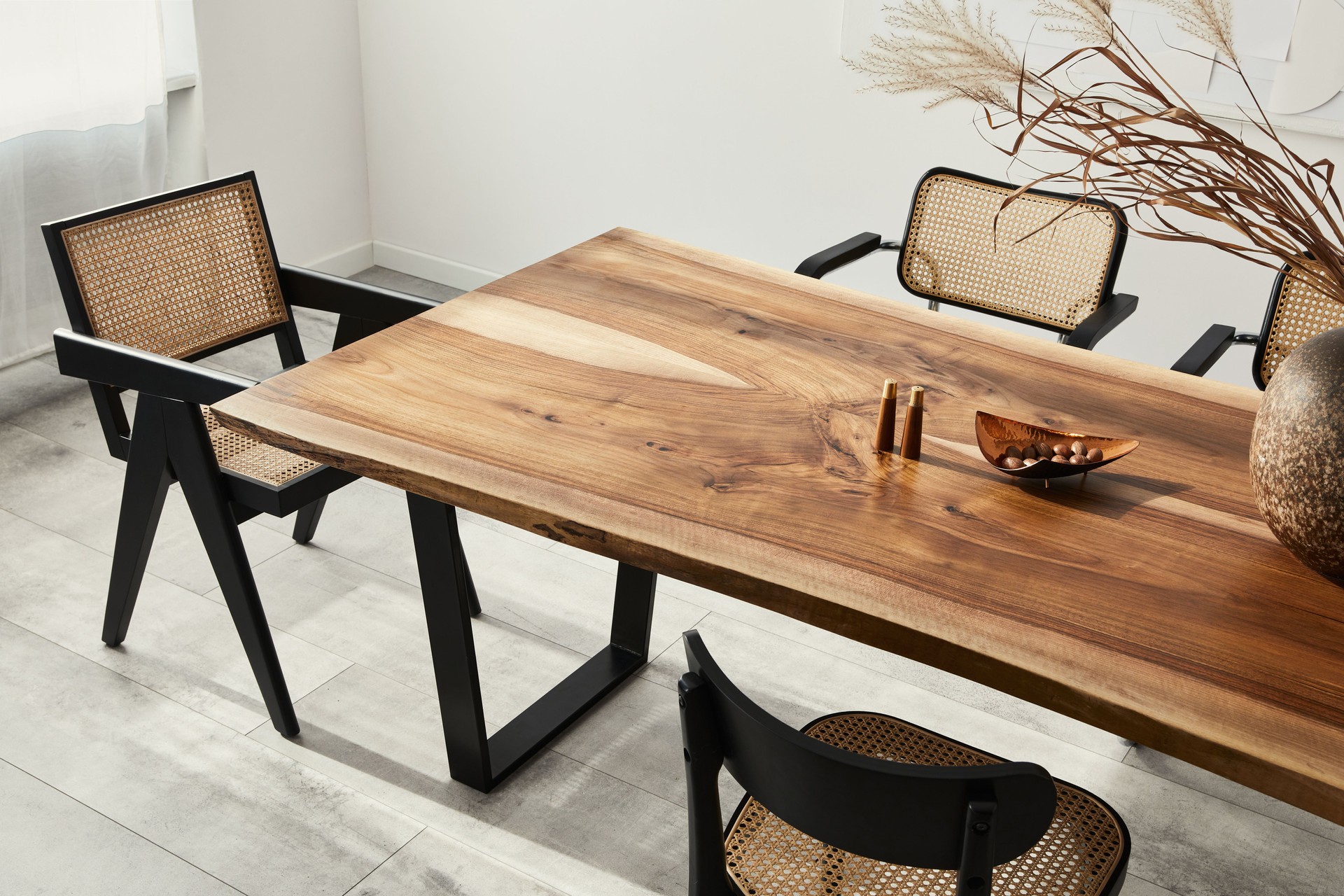 Interior design of stylish dining room interior with family wooden table, modern chairs, plate with nuts, salt and pepper shakers. Concrete floor. White wall. Template.